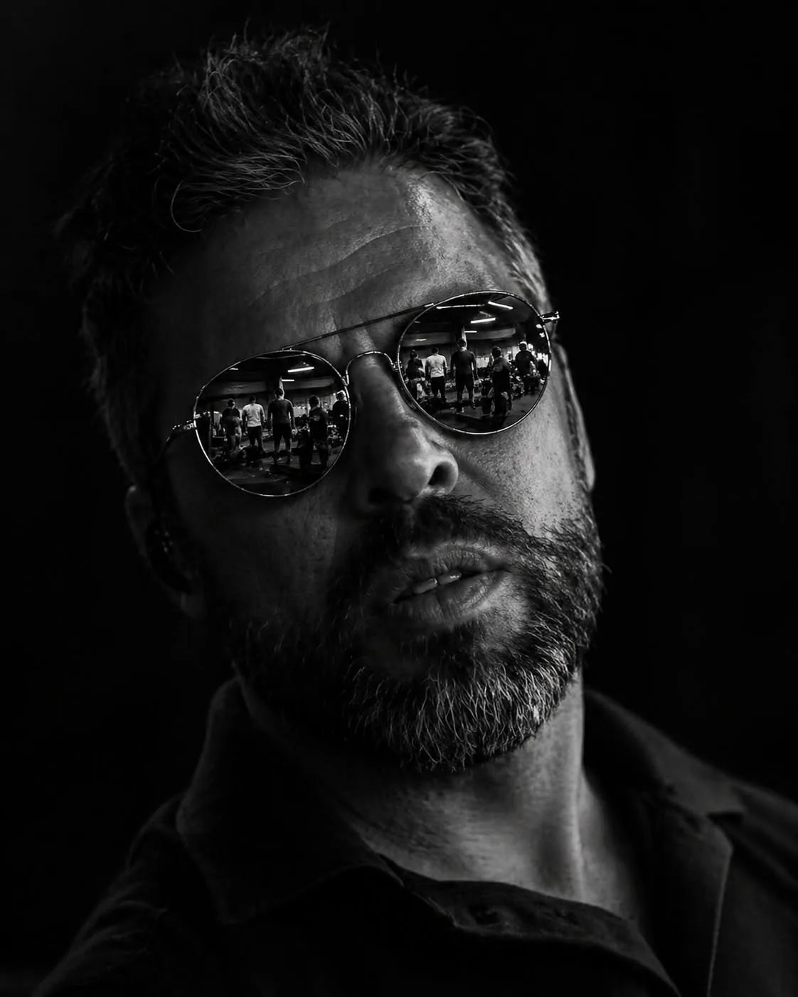 Retrato de Paulo Serrano, a preto e branco, com óculos escuros onde se reflecte um ginásio.